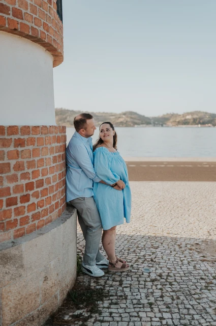 Together beside the curved waterfront wall | Lisbon engagement photoshoot The couple leaning close together beside a curved red-brick and white wall on the waterfront during their engagement photoshoot in Lisbon.