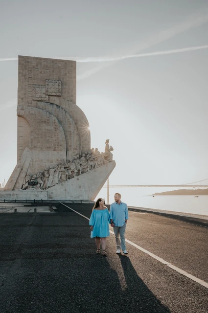 A walk by the Monument to the Discoveries | Lisbon engagement photoshoot The couple holding hands on the waterfront with the Monument to the Discoveries behind them during their engagement photoshoot in Lisbon.