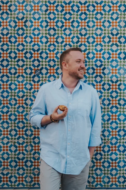A pastry portrait beside the tiles | Lisbon engagement photoshoot The man smiling with a custard tart in his hand beside the tile wall during their engagement photoshoot in Lisbon.
