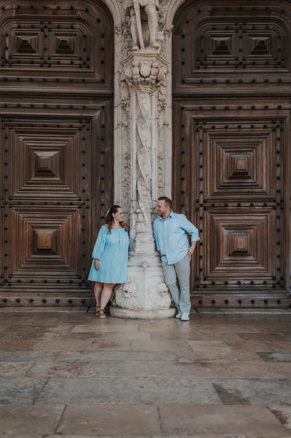 A portrait between the monastery doors | Lisbon engagement photoshoot The couple leaning on either side of a carved stone column between the monastery’s wooden doors during their engagement photoshoot in Lisbon.