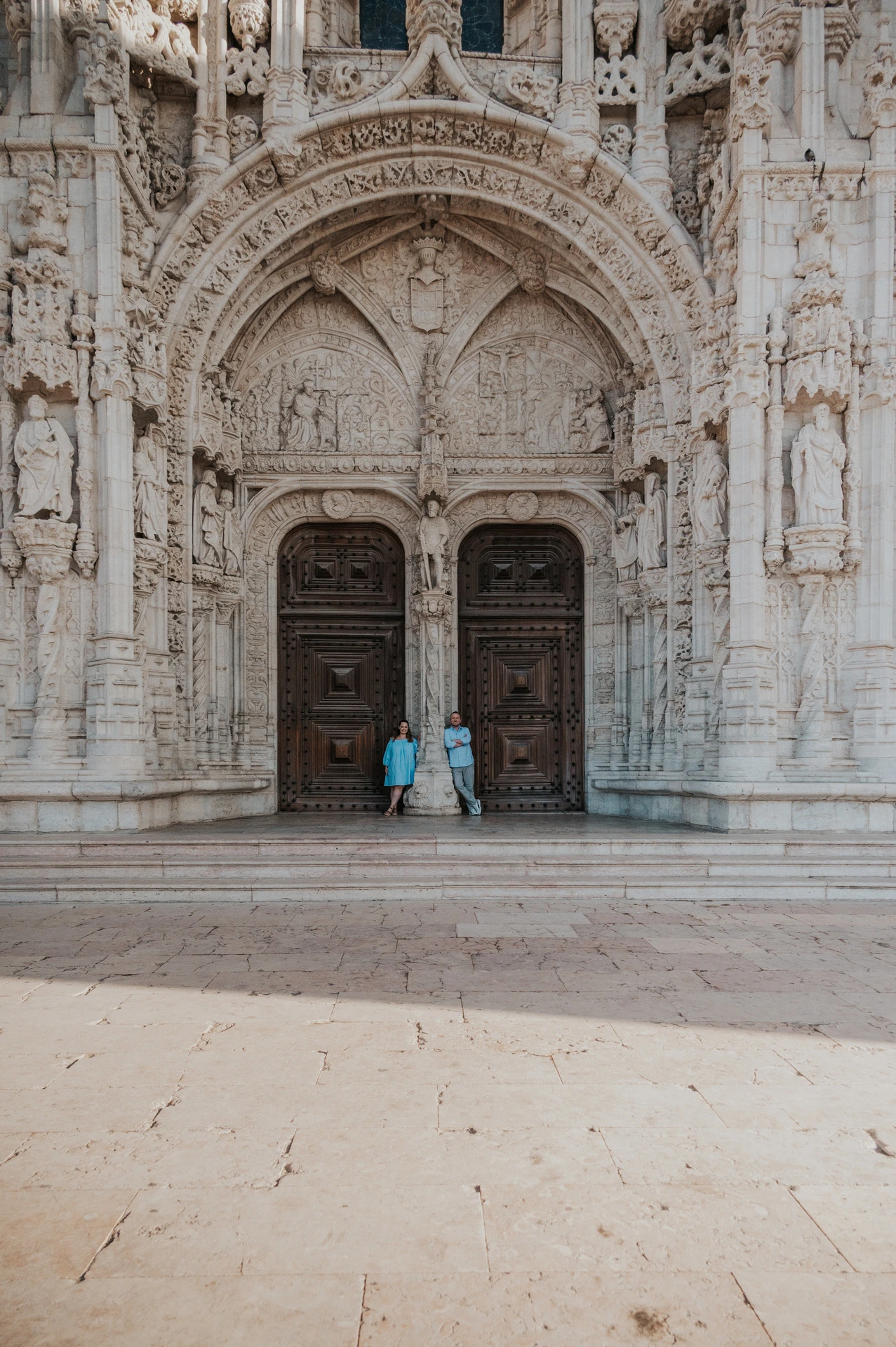 A wide view of the couple beneath the ornate entrance of Jerónimos Monastery during their engagement photoshoot in Lisbon.