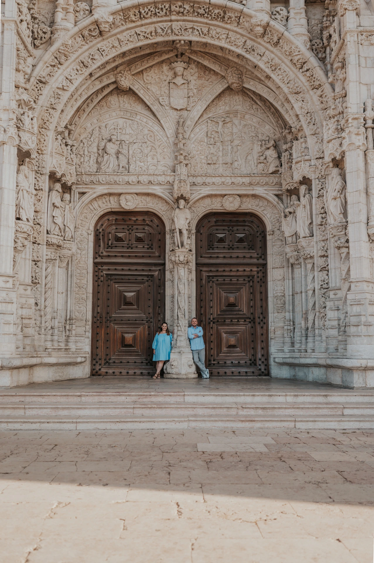 A wide view of the couple beneath the ornate entrance of Jerónimos Monastery during their engagement photoshoot in Lisbon.