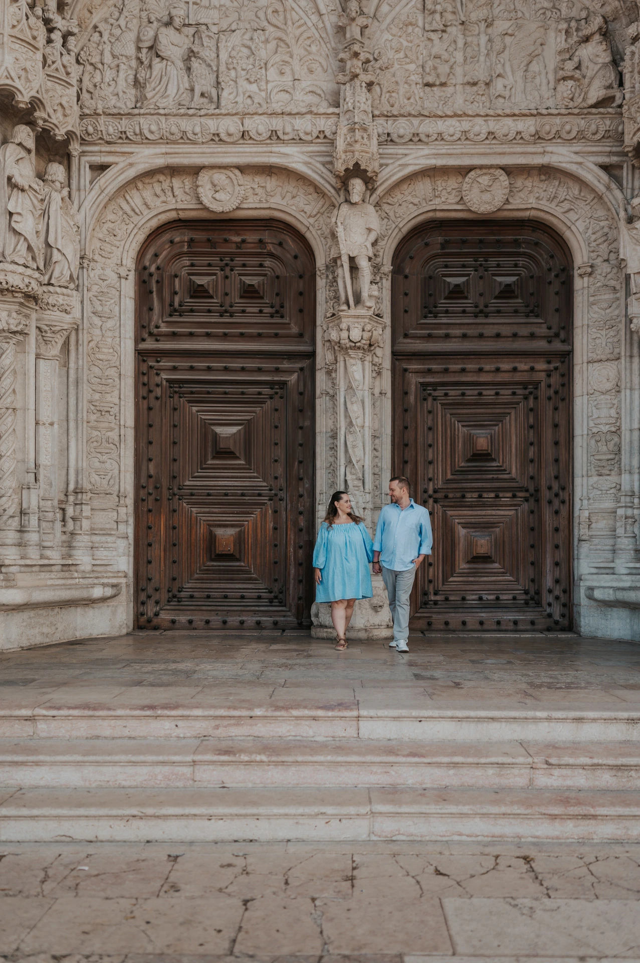 The couple holding hands and moving together on the steps outside Jerónimos Monastery during their engagement photoshoot in Lisbon.