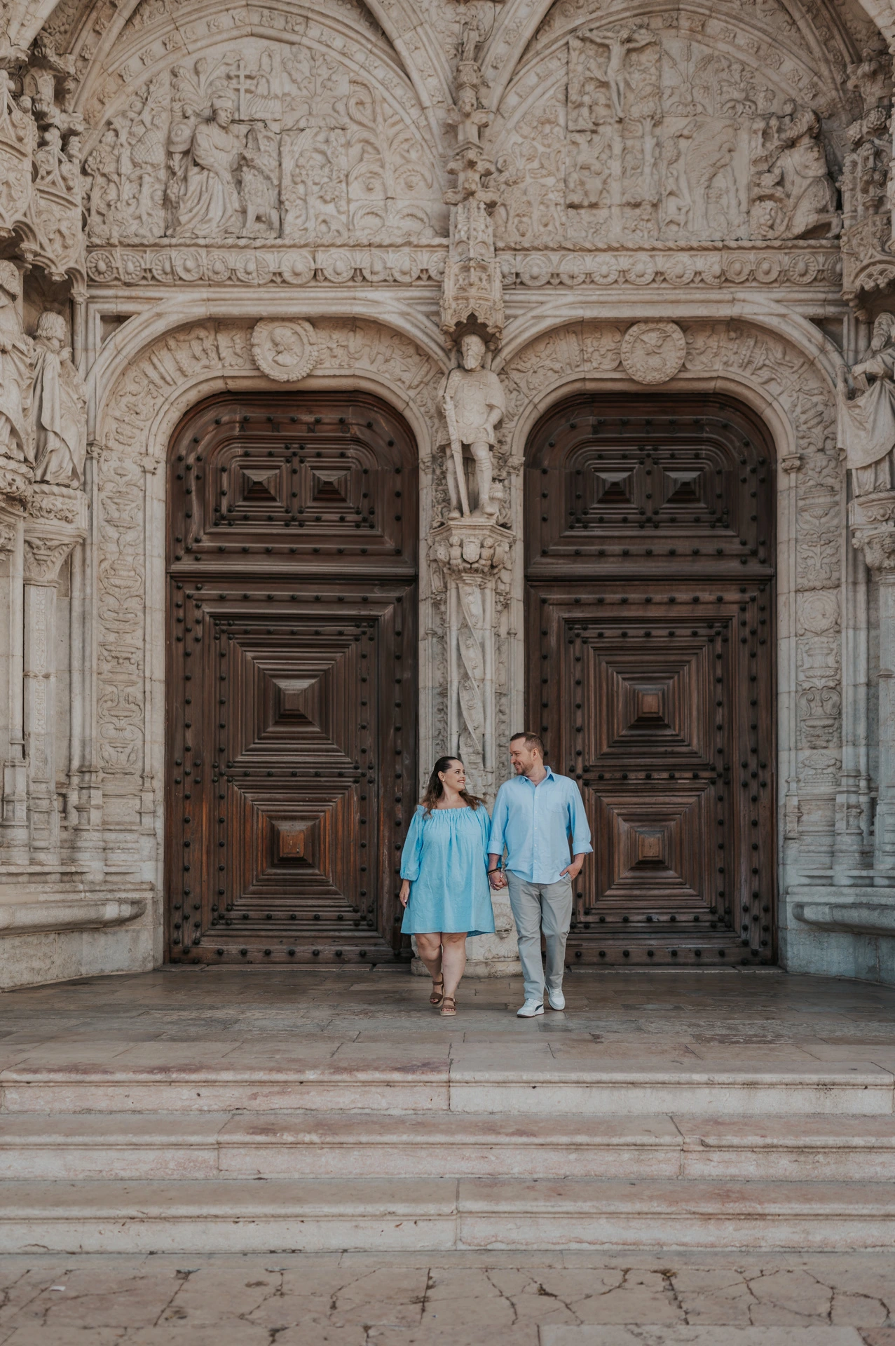 The couple holding hands and moving together on the steps outside Jerónimos Monastery during their engagement photoshoot in Lisbon.