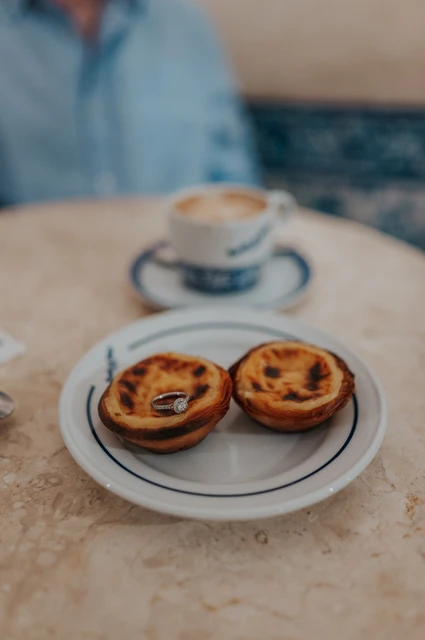 Pastéis and coffee at the café | Lisbon engagement photoshoot Two custard tarts on a café table with a cup of coffee behind them during their engagement photoshoot in Lisbon.