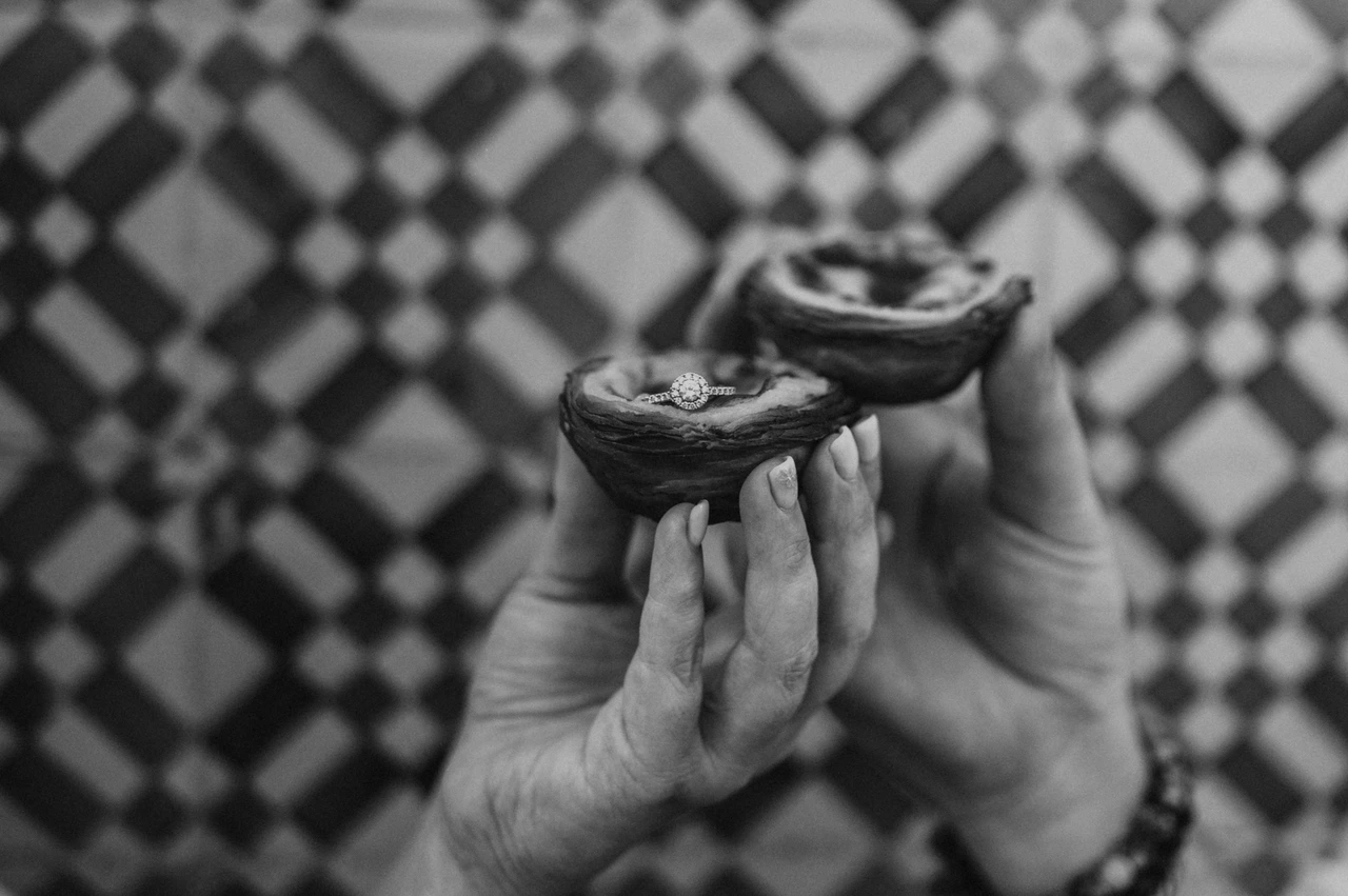 Two pastéis held up against the tiles in black and white | Lisbon engagement photoshoot Black-and-white photograph: the couple holding two custard tarts together in front of the colourful patterned tiles during their engagement photoshoot in Lisbon.