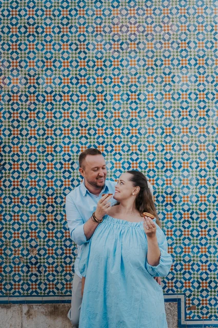 Sharing a pastry and a smile | Lisbon engagement photoshoot The man holding a custard tart towards his smiling partner beside the tile wall during their engagement photoshoot in Lisbon.