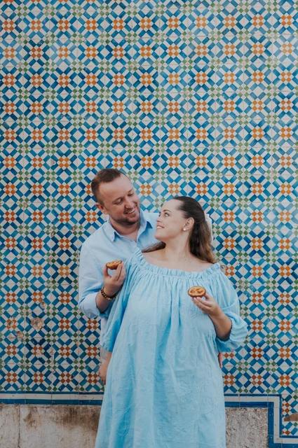 Sharing a pastry and a smile | Lisbon engagement photoshoot The man holding a custard tart towards his smiling partner beside the tile wall during their engagement photoshoot in Lisbon.