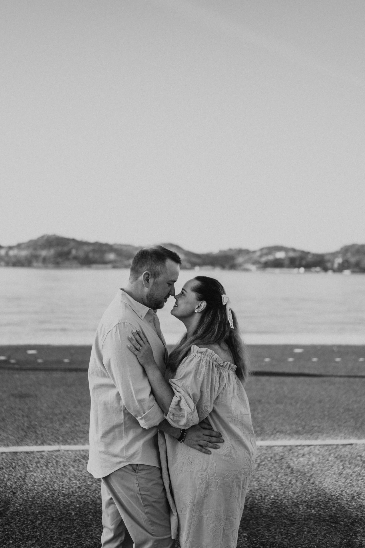 Black-and-white photograph: the couple holding each other face to face beside the river during their engagement photoshoot in Lisbon.