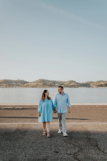 Hand in hand beside the river | Lisbon engagement photoshoot The couple walking hand in hand with the river stretching out behind them during their engagement photoshoot in Lisbon.