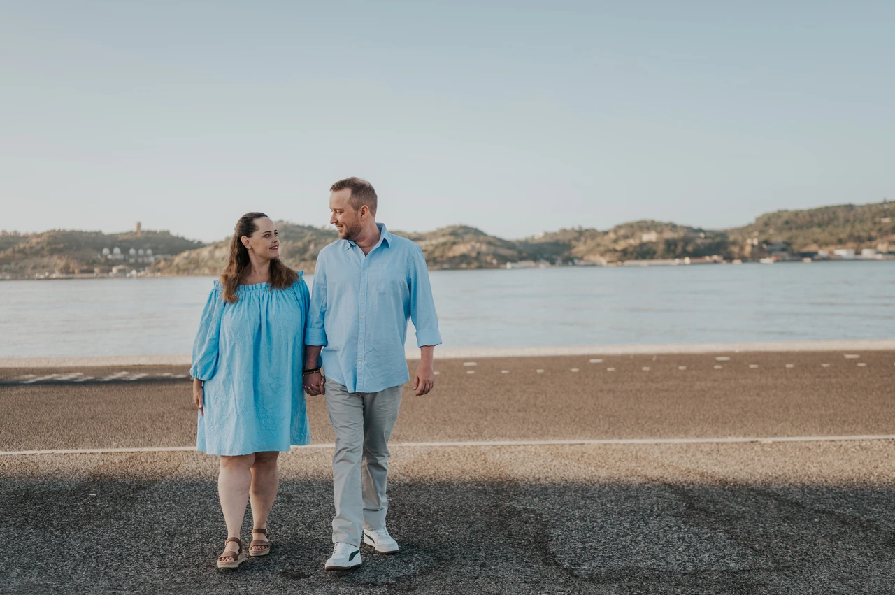 Hand in hand beside the river | Lisbon engagement photoshoot The couple walking hand in hand with the river stretching out behind them during their engagement photoshoot in Lisbon.