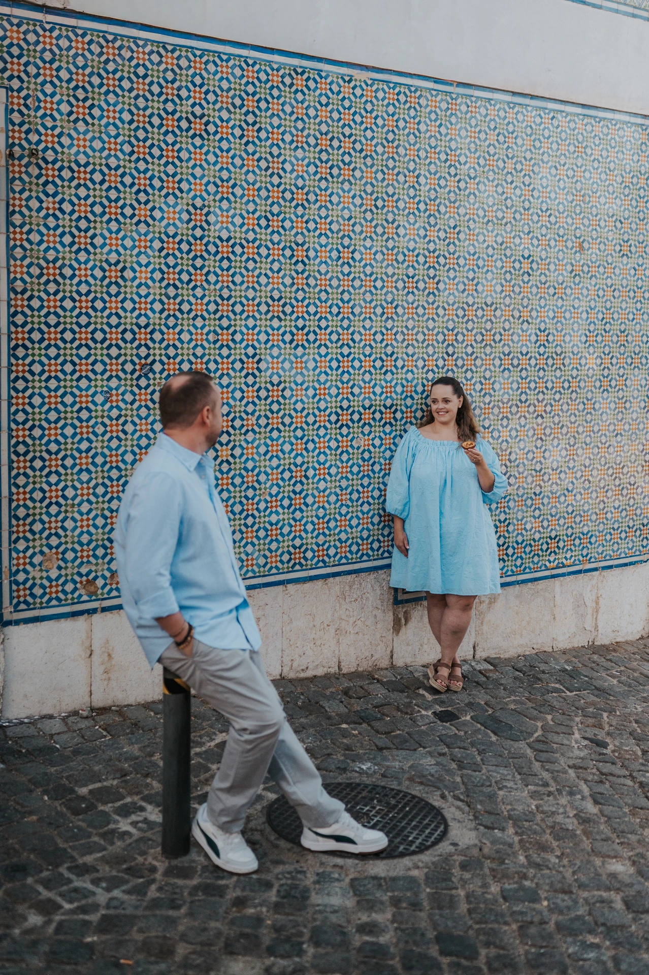 The couple leaning apart against the long patterned tile wall during their engagement photoshoot in Lisbon.