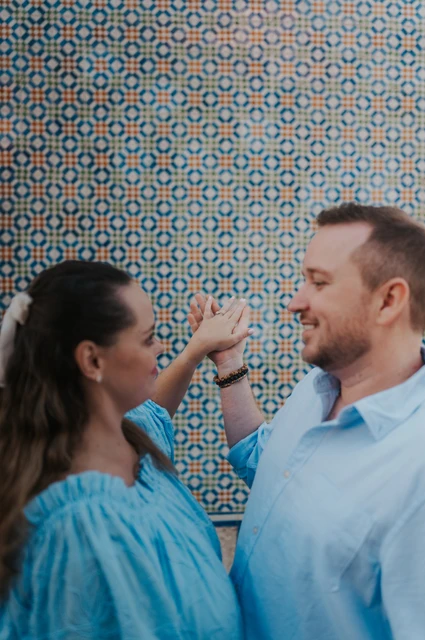 A playful hand-in-hand portrait | Lisbon engagement photoshoot The couple facing each other with their joined hands raised near their faces by the tile wall during their engagement photoshoot in Lisbon.