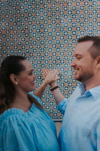 A playful hand-in-hand portrait | Lisbon engagement photoshoot The couple facing each other with their joined hands raised near their faces by the tile wall during their engagement photoshoot in Lisbon.