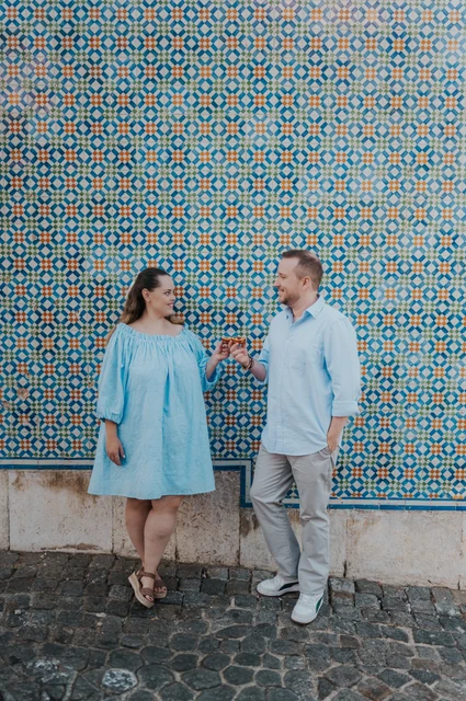 Pastries beside the patterned tiles | Lisbon engagement photoshoot The couple smiling together with pastries in front of a blue and yellow patterned tile wall during their engagement photoshoot in Lisbon.