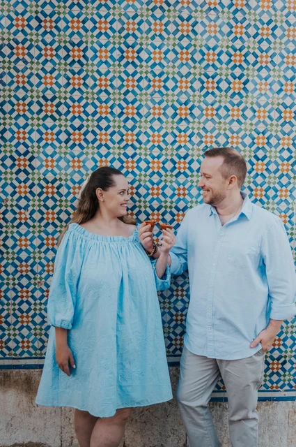 Pastries beside the patterned tiles | Lisbon engagement photoshoot The couple smiling together with pastries in front of a blue and yellow patterned tile wall during their engagement photoshoot in Lisbon.