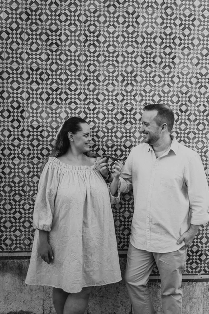 Pastries beside the patterned tiles in black and white | Lisbon engagement photoshoot Black-and-white photograph: the couple smiling together with pastries in front of a blue and yellow patterned tile wall during their engagement photoshoot in Lisbon.