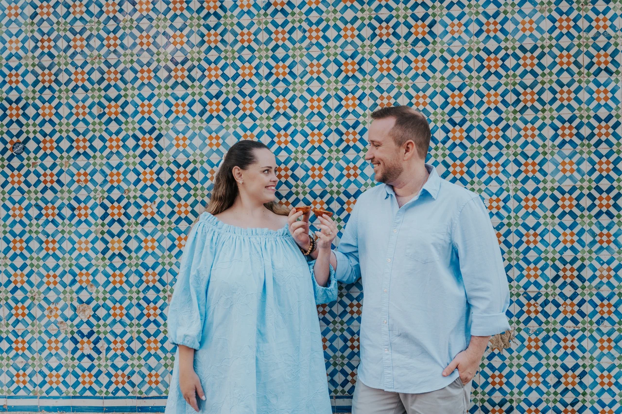 Pastries beside the patterned tiles | Lisbon engagement photoshoot The couple smiling together with pastries in front of a blue and yellow patterned tile wall during their engagement photoshoot in Lisbon.