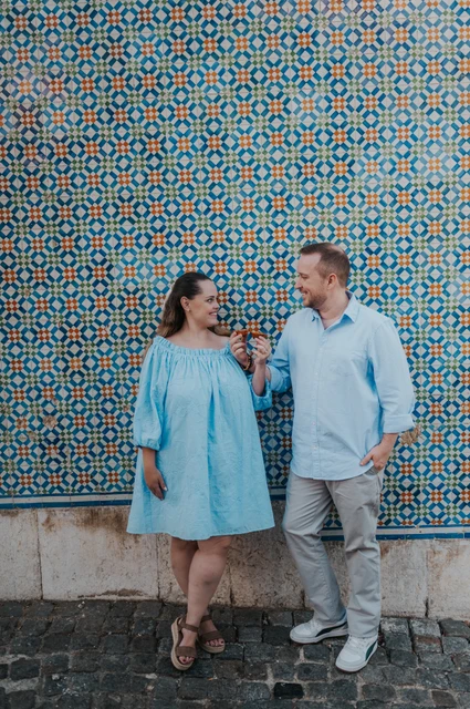 Pastries beside the patterned tiles | Lisbon engagement photoshoot The couple smiling together with pastries in front of a blue and yellow patterned tile wall during their engagement photoshoot in Lisbon.