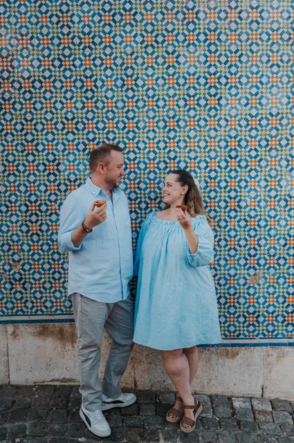 Pastries beside the patterned tiles | Lisbon engagement photoshoot The couple smiling together with pastries in front of a blue and yellow patterned tile wall during their engagement photoshoot in Lisbon.
