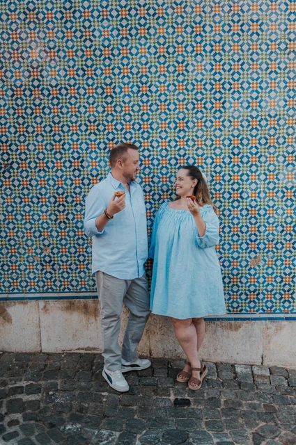 Pastries beside the patterned tiles | Lisbon engagement photoshoot The couple smiling together with pastries in front of a blue and yellow patterned tile wall during their engagement photoshoot in Lisbon.