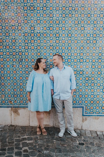 Pastries beside the patterned tiles | Lisbon engagement photoshoot The couple smiling together with pastries in front of a blue and yellow patterned tile wall during their engagement photoshoot in Lisbon.