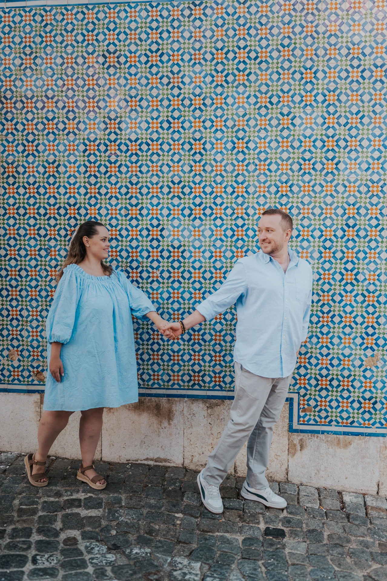 The couple reaching towards each other with joined hands against the patterned tiles during their engagement photoshoot in Lisbon.