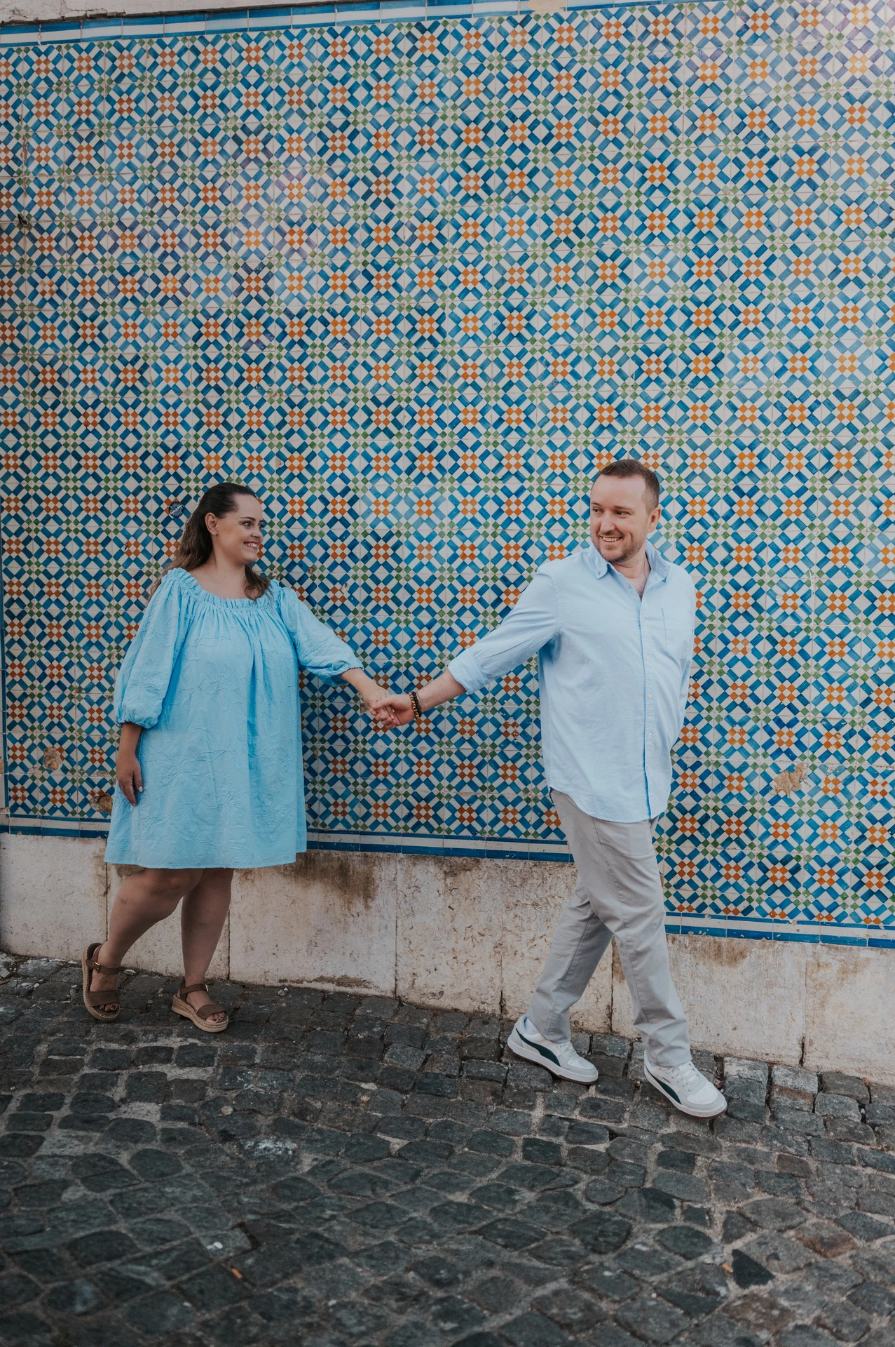 The couple reaching towards each other with joined hands against the patterned tiles during their engagement photoshoot in Lisbon.