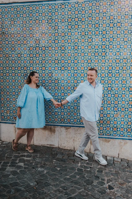 Joined hands along the tile wall | Lisbon engagement photoshoot The couple reaching towards each other with joined hands against the patterned tiles during their engagement photoshoot in Lisbon.