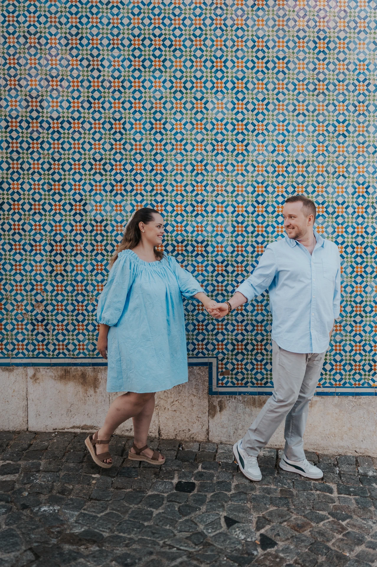 The couple reaching towards each other with joined hands against the patterned tiles during their engagement photoshoot in Lisbon.