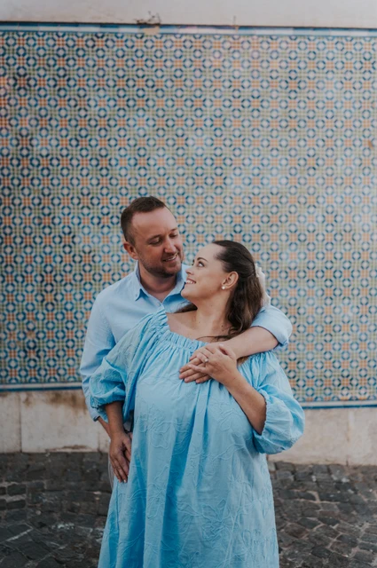 A smiling embrace beside the tile wall | Lisbon engagement photoshoot The man with an arm around his partner’s shoulder as they smile at each other against the tiles during their engagement photoshoot in Lisbon.