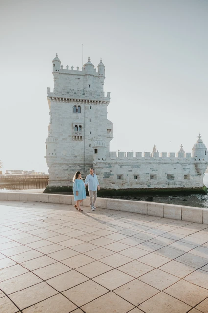 Walking together beside Belém Tower | Lisbon engagement photoshoot The couple walking across the waterfront paving with Belém Tower behind them during their engagement photoshoot in Lisbon.