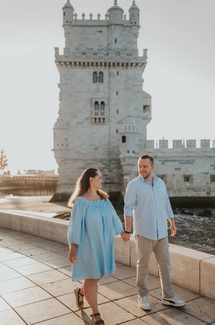 Walking together beside Belém Tower | Lisbon engagement photoshoot The couple walking across the waterfront paving with Belém Tower behind them during their engagement photoshoot in Lisbon.