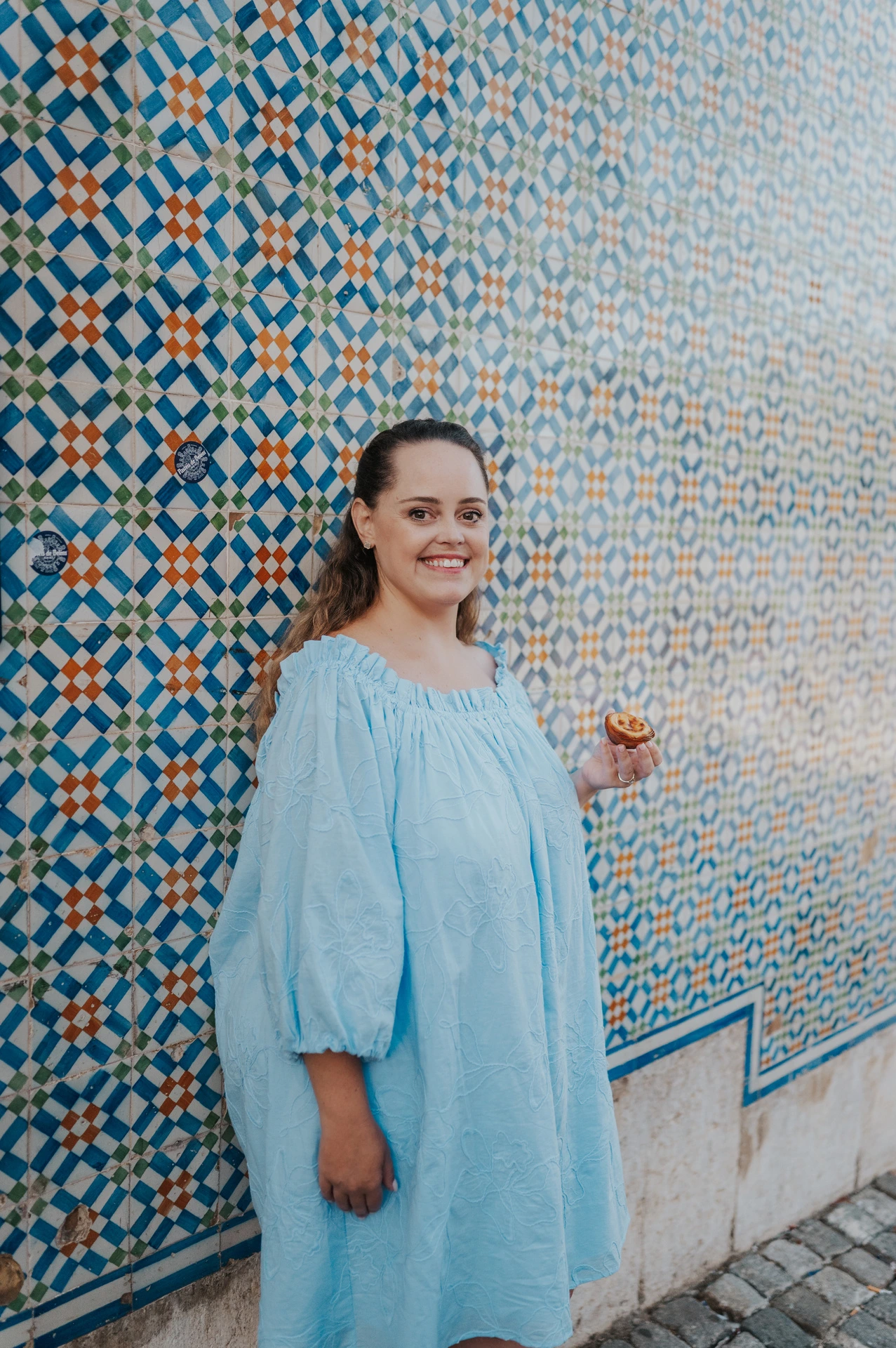 The woman smiling beside the patterned tile wall during their engagement photoshoot in Lisbon.