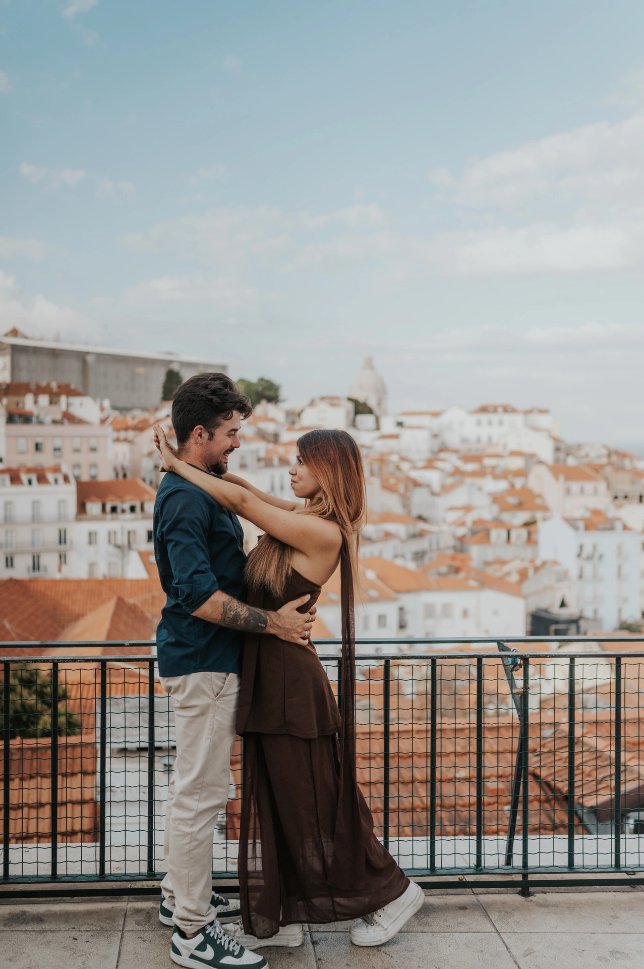 The woman wrapping her arms around her partner’s shoulders at Portas do Sol during their engagement photoshoot in Lisbon.