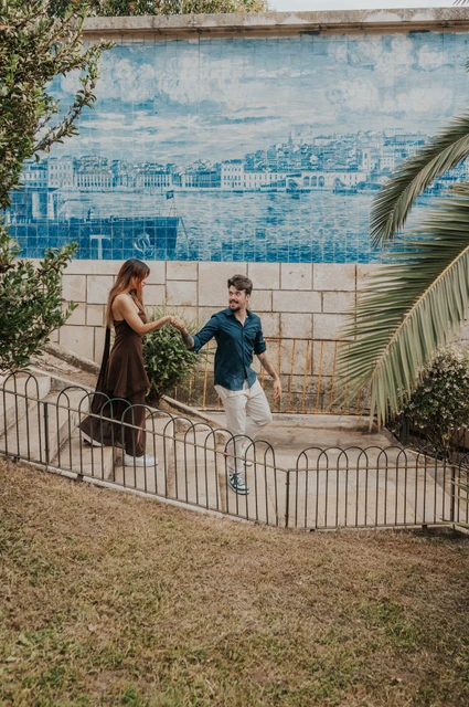 Holding hands on the blue-tiled stairway | Lisbon engagement photoshoot The couple holding hands on the steps beside a large blue tile panel at Santa Luzia during their engagement photoshoot in Lisbon.
