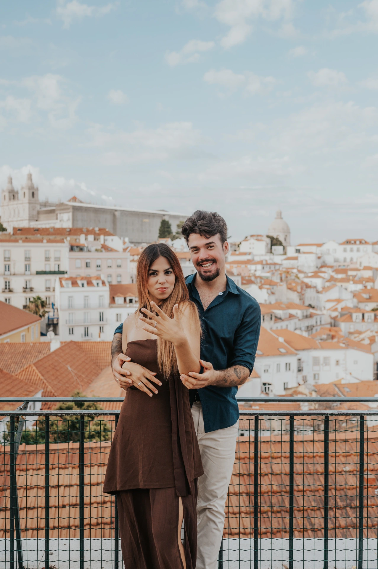 The couple facing the camera with his arms around her at Portas do Sol during their engagement photoshoot in Lisbon.
