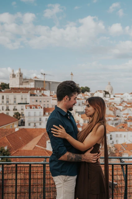 Together above the Portas do Sol rooftops | Lisbon engagement photoshoot A vertical portrait of the couple holding each other above the rooftops at Portas do Sol during their engagement photoshoot in Lisbon.