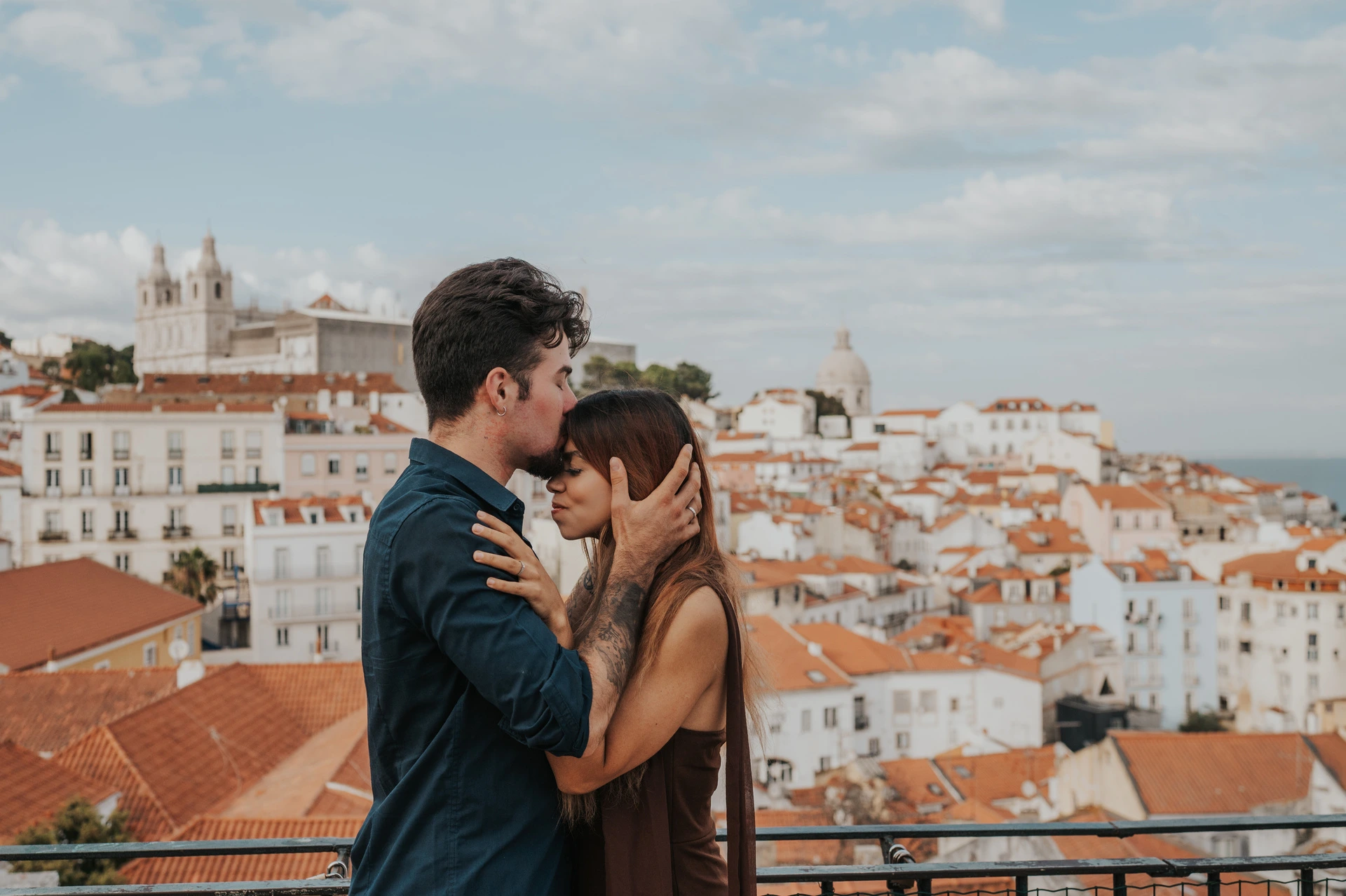 A forehead kiss above the terracotta rooftops at Portas do Sol during their engagement photoshoot in Lisbon.