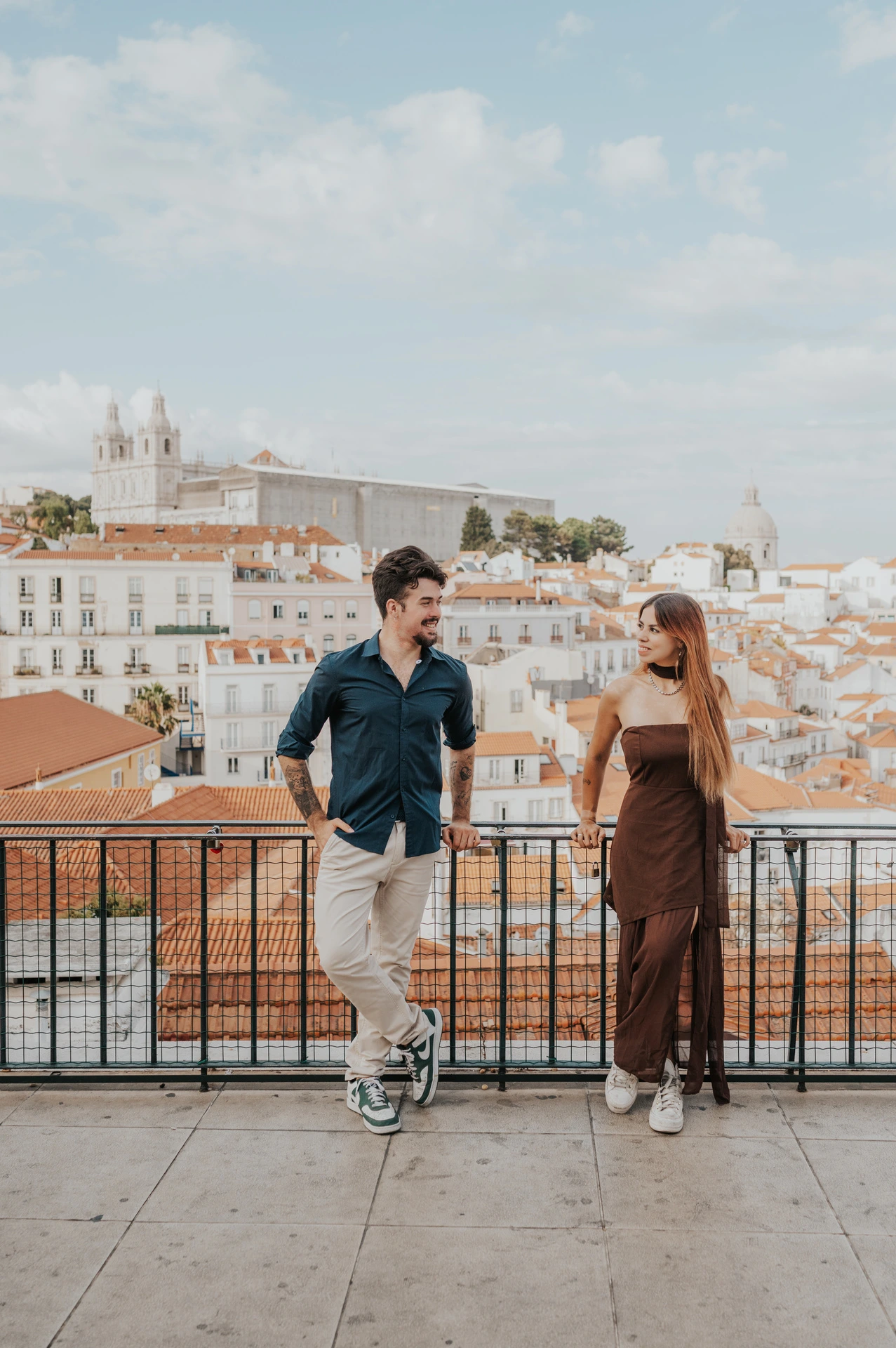 A full-length portrait of the couple leaning against the Portas do Sol railing during their engagement photoshoot in Lisbon.