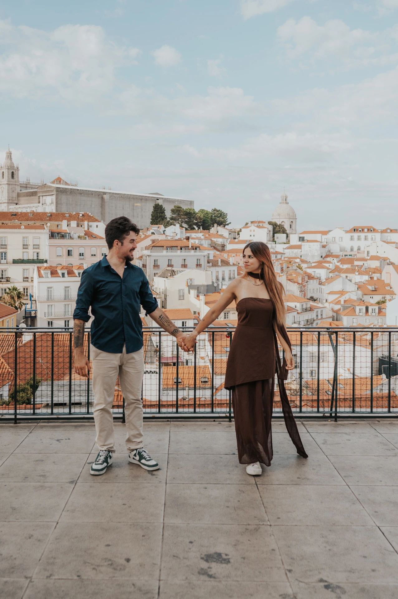 The couple stepping apart while holding hands at Portas do Sol during their engagement photoshoot in Lisbon.