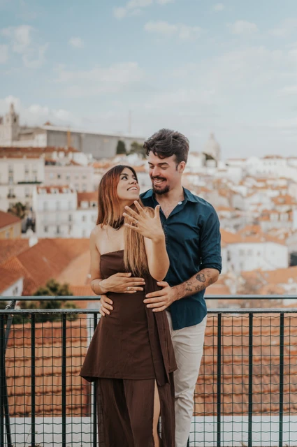 Looking up with her ring hand raised | Lisbon engagement photoshoot The woman looking up at her partner while holding her ring hand near her face at Portas do Sol during their engagement photoshoot in Lisbon.