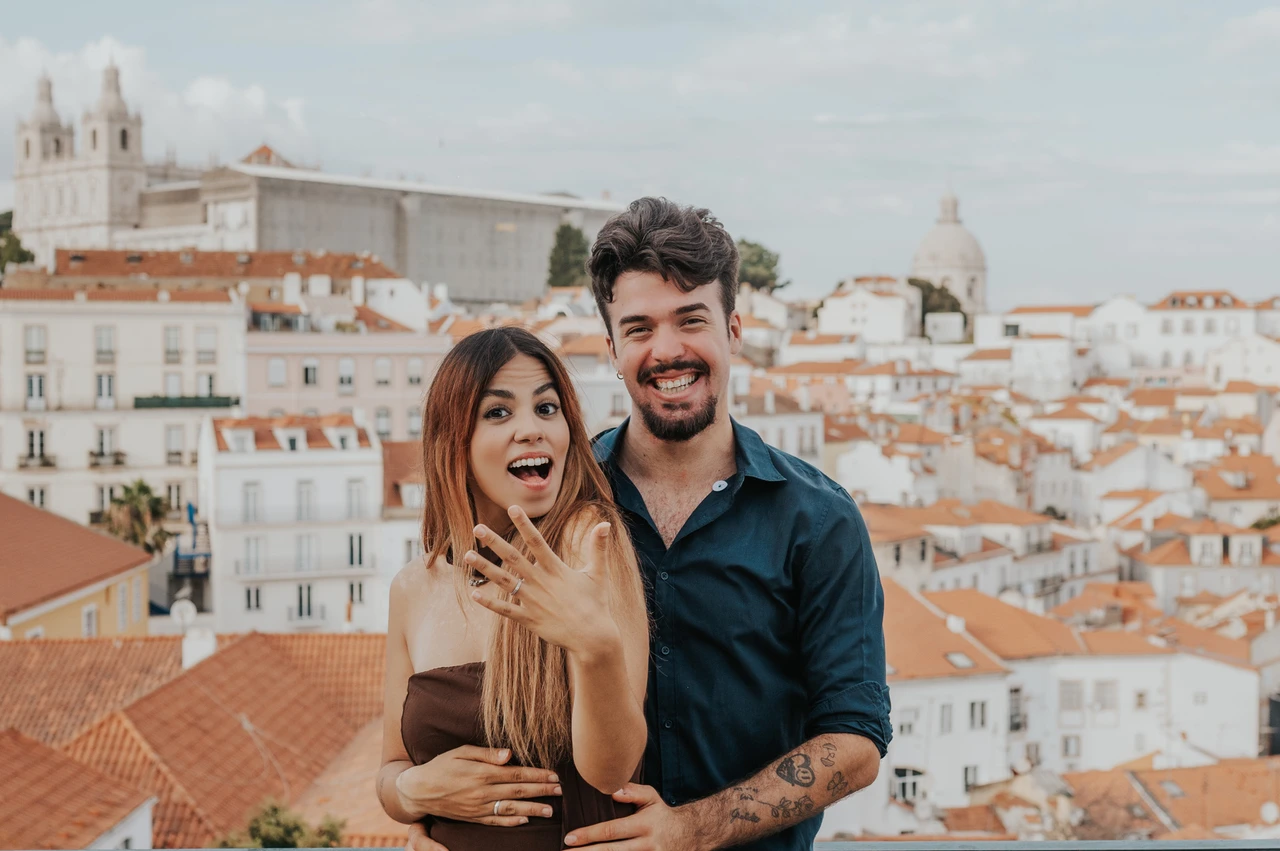 Celebrating their engagement above the rooftops | Lisbon engagement photoshoot The couple smiling towards the camera as she holds up her engagement ring at Portas do Sol during their engagement photoshoot in Lisbon.