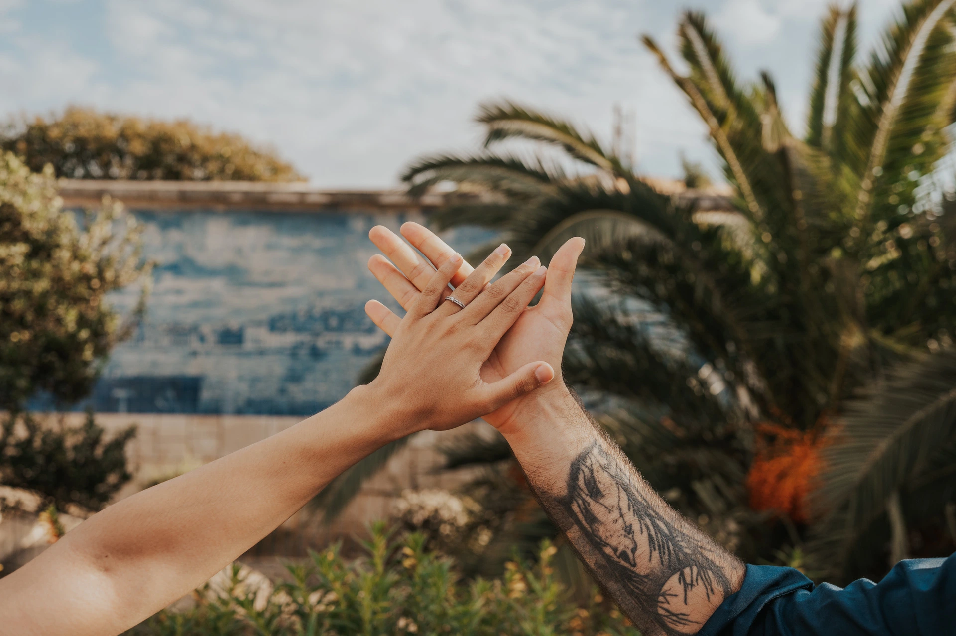 A close-up of the couple’s hands and engagement ring with blue tiles and palms behind them at Santa Luzia during their engagement photoshoot in Lisbon.