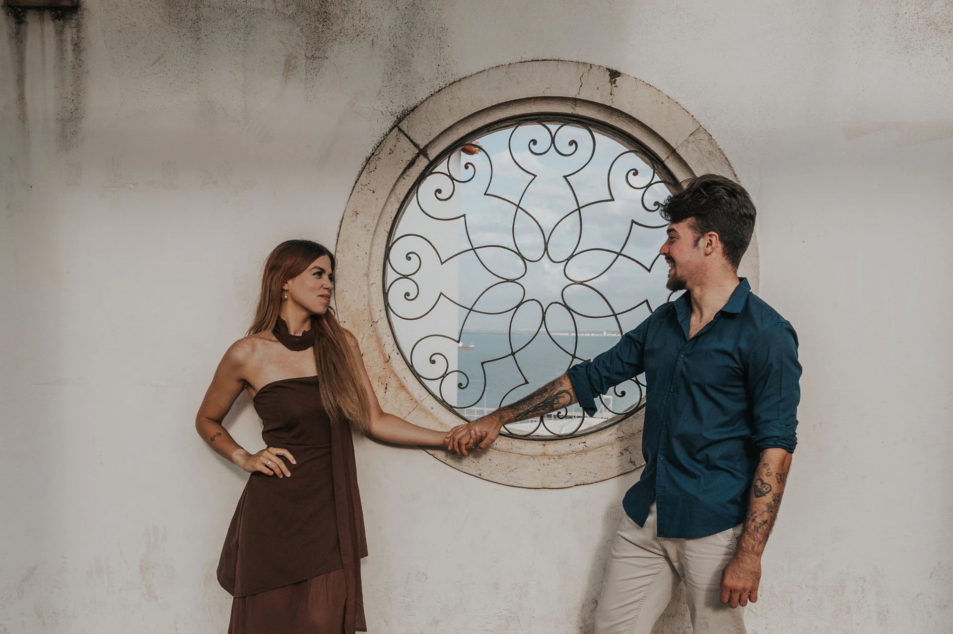 A closer view of the couple holding hands beside the circular window at Santa Luzia during their engagement photoshoot in Lisbon.