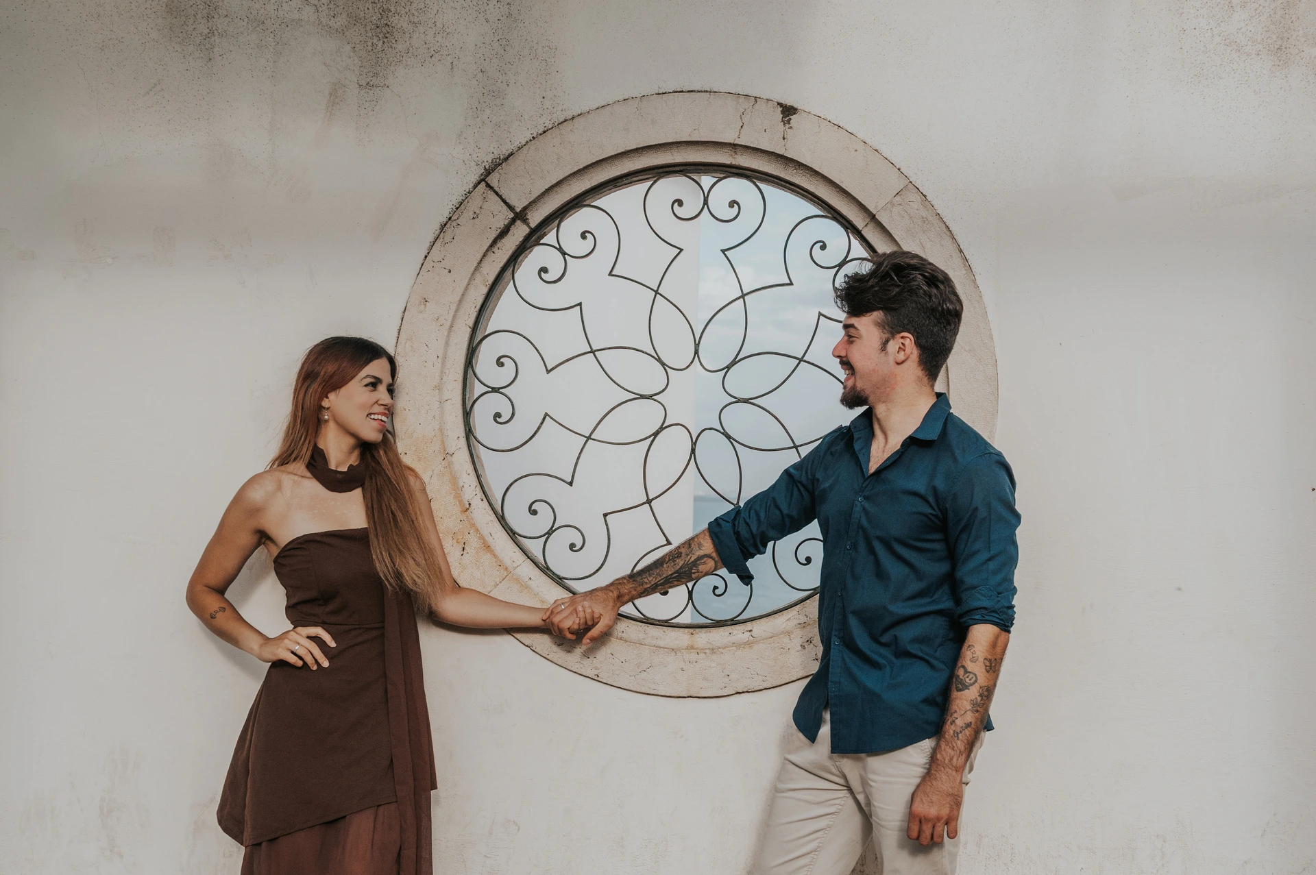 The couple holding hands in front of a circular window at Santa Luzia during their engagement photoshoot in Lisbon.