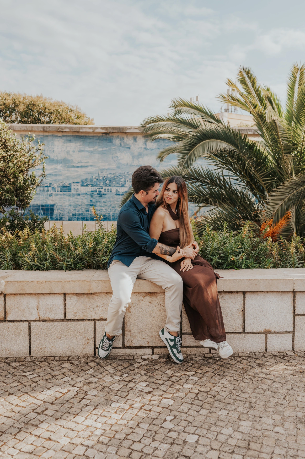 A cheek kiss while the couple sit on the garden wall at Santa Luzia during their engagement photoshoot in Lisbon.