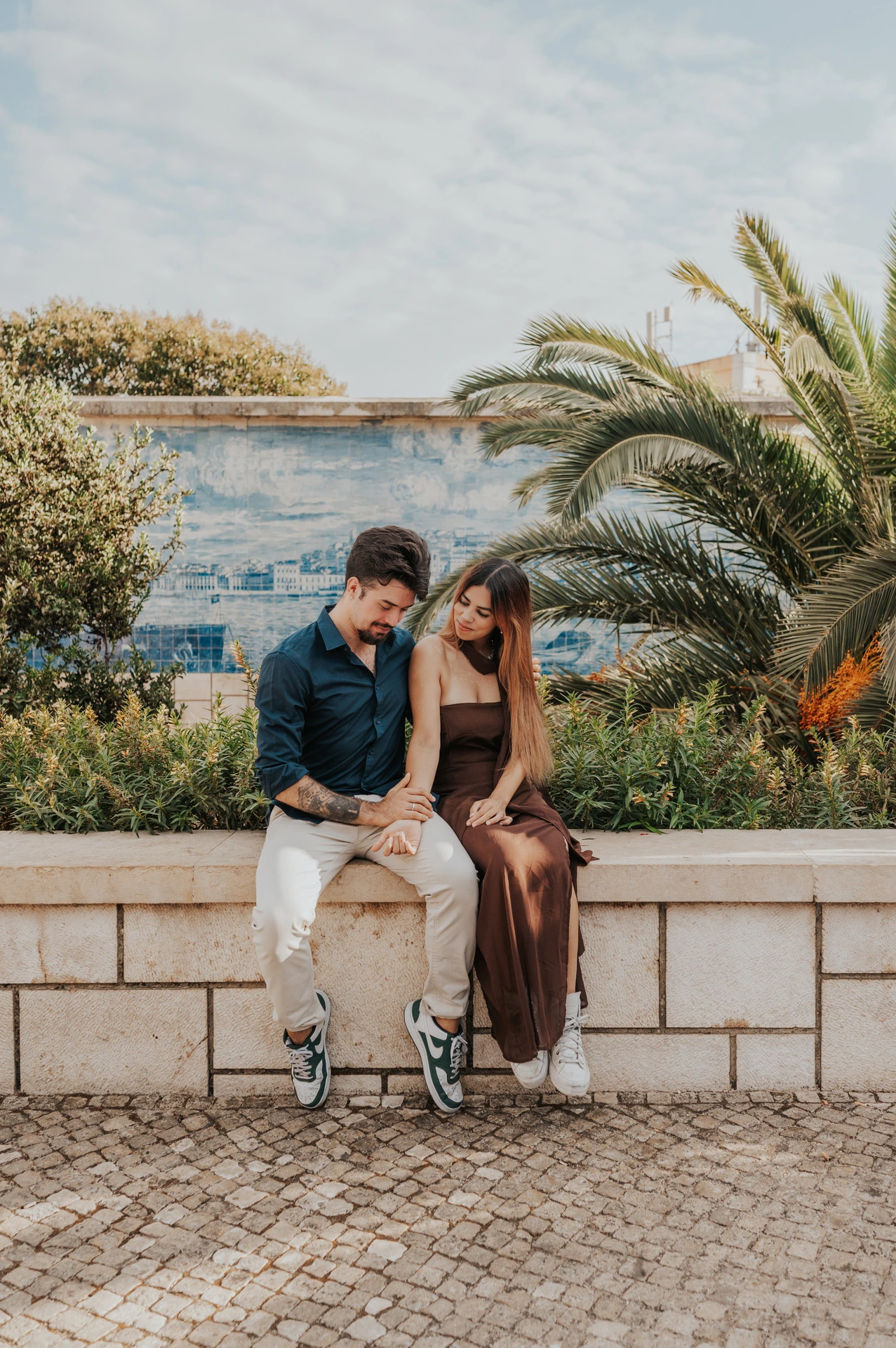 The seated couple looking down at their joined hands at Santa Luzia during their engagement photoshoot in Lisbon.