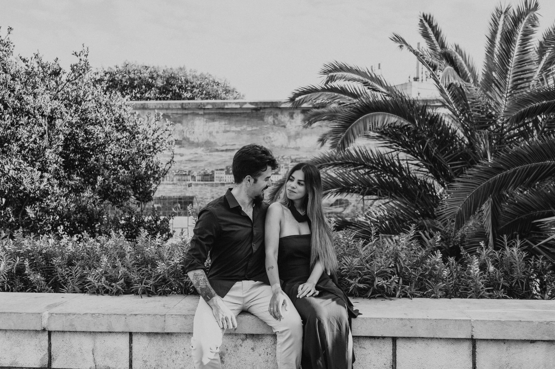 A black-and-white portrait of the seated couple beside the palms and tiled wall at Santa Luzia during their engagement photoshoot in Lisbon.