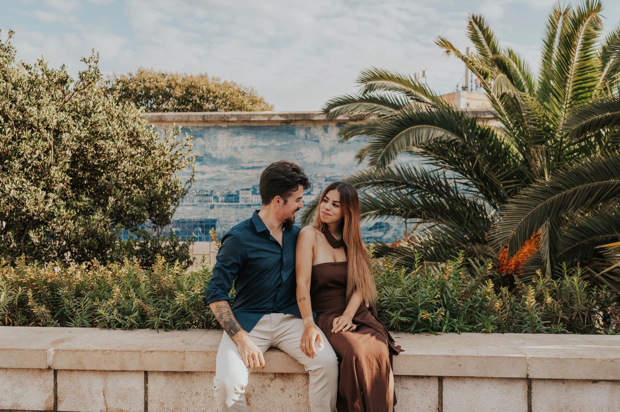 Seated together beneath the palms | Lisbon engagement photoshoot A wide portrait of the couple sitting together beneath the palms at Santa Luzia during their engagement photoshoot in Lisbon.